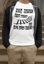 A confident man standing on a staircase wearing a white 'Hey There, Train Wreck, This Isn't Your Station' tee